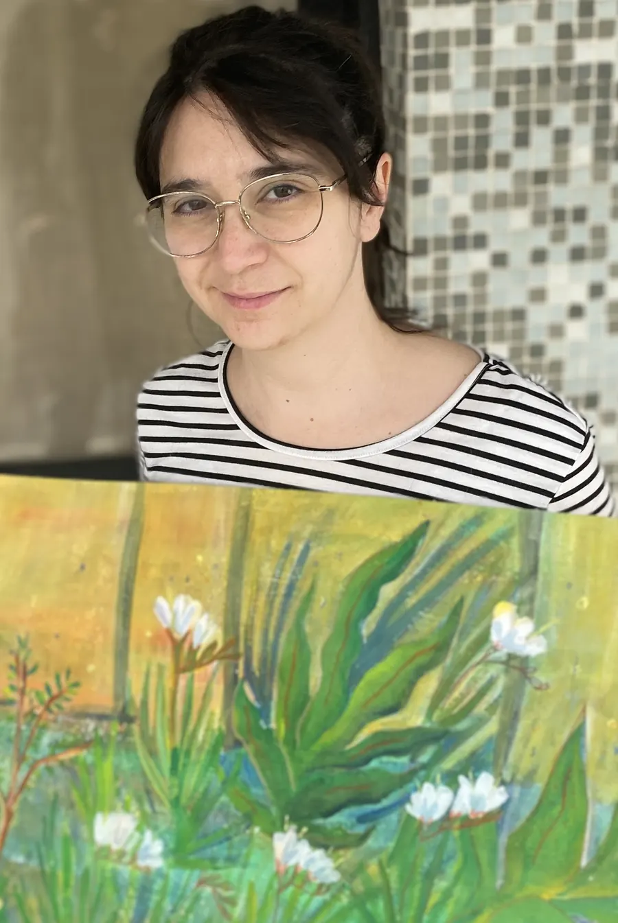 Nat smiling behind one of her paintings: green leaves and white flowers on a yellow background.